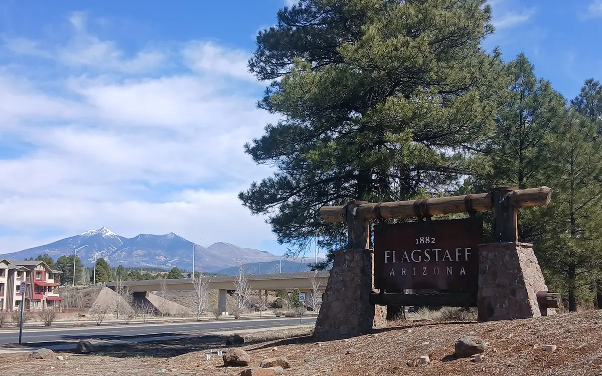 A Welcome to Flagstaff sign with the snow-dusted San Francisco Peaks behind it in Flagstaff, Arizona